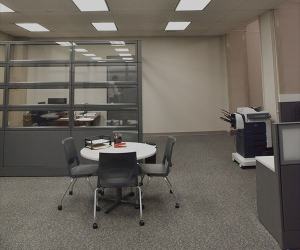 An office space with a round table, 4 chairs and a desk behind a glass screen