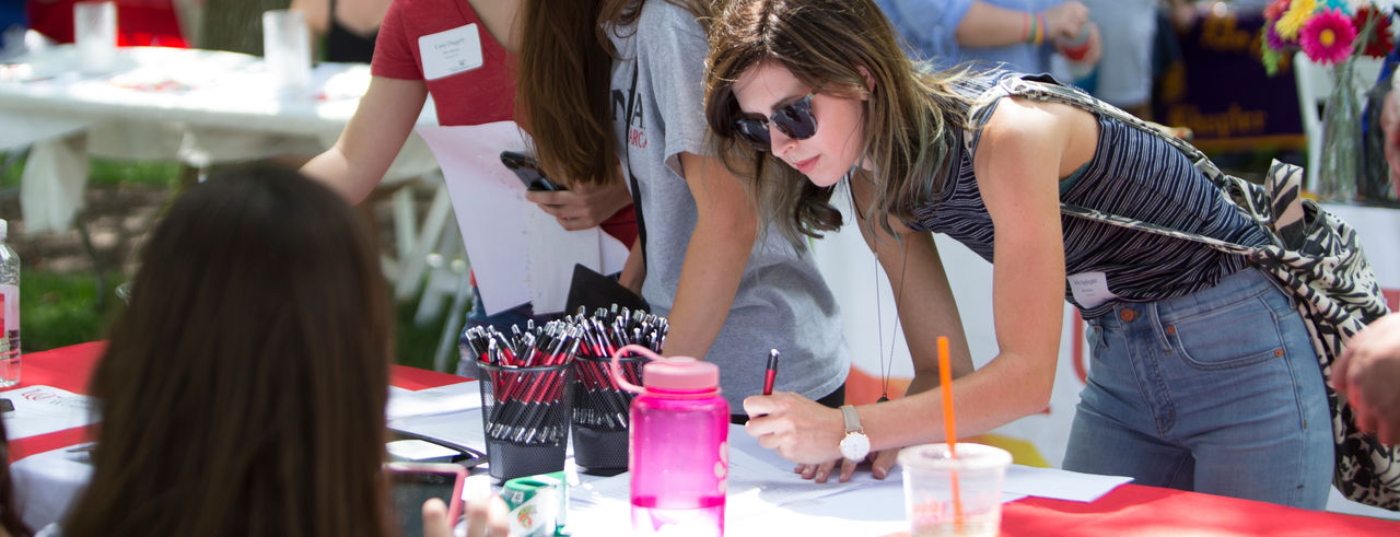 a student leans down over a table to sign a paper during new student orientation