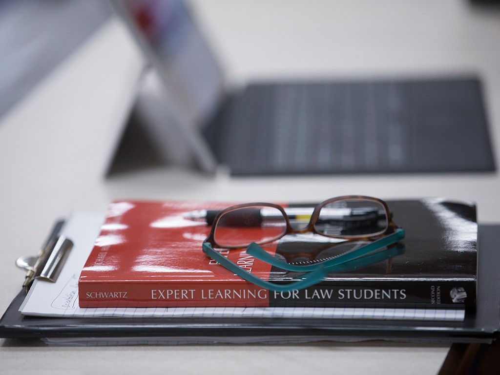 A pair of glasses rest on top of a stack of books in a College of Law classroom.